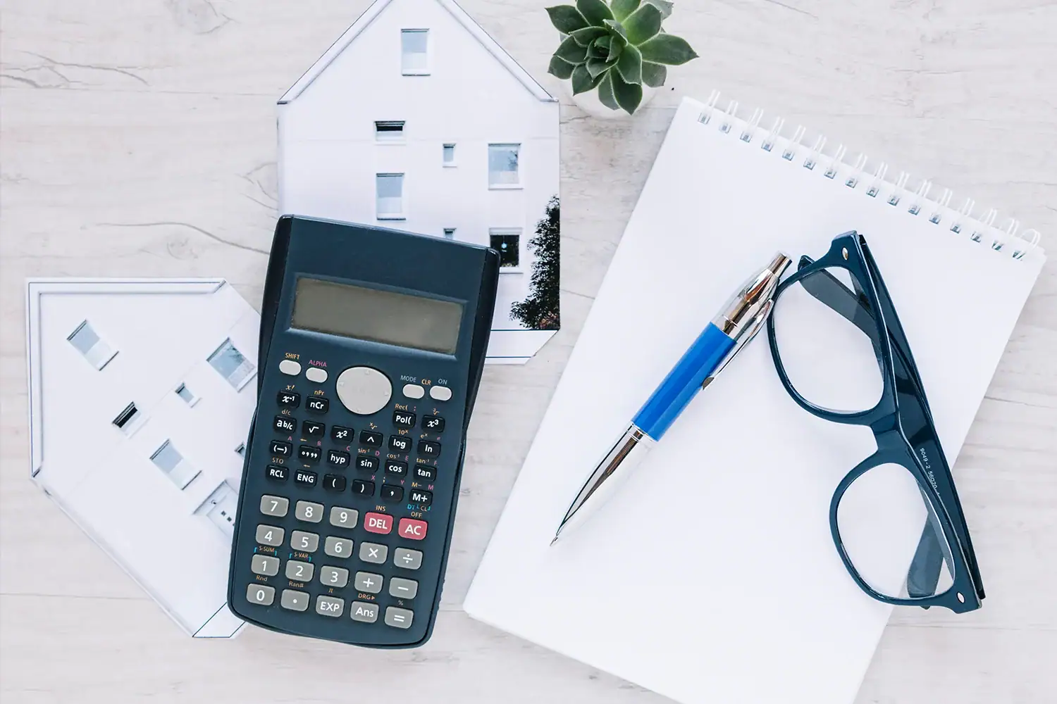 Calculator, house model, and notepad on desk, representing property tax assessment review and protest services by Tax Cutter in Texas.