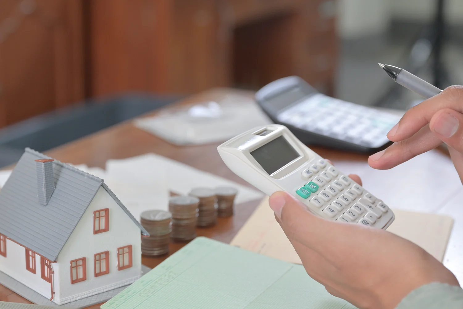 Homeowner calculating property taxes with a calculator and house model, representing Texas property tax protest and savings services by Tax Cutter.