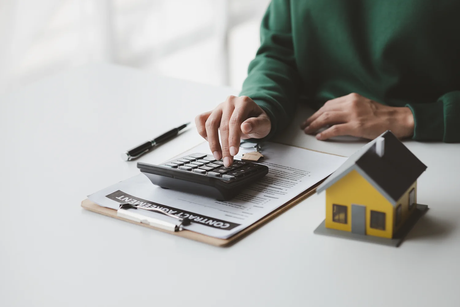 Homeowner calculating property taxes with a calculator beside a house model and contract, representing Texas property tax protest services by Tax Cutter.