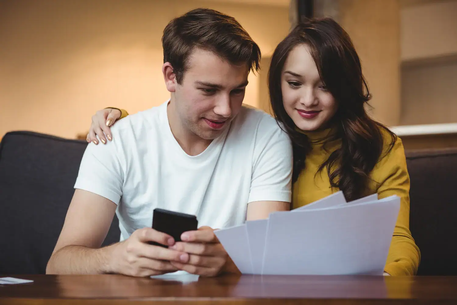 A happy couple reviewing property tax documents and checking savings on a phone, representing Houston property tax protest services by Tax Cutter.
